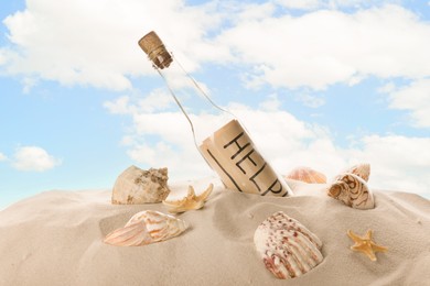 Corked glass bottle with Help note and seashells on sand against sky