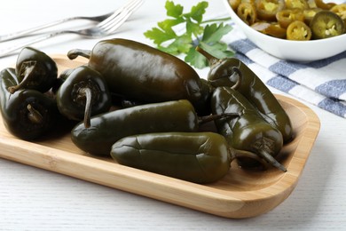 Photo of Wooden tray with pickled green jalapeno peppers on white table