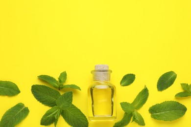 Bottle of essential oil and mint on yellow background, flat lay. Space for text