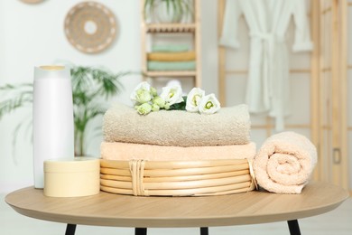 Soft folded towels, cosmetic products and flowers on wooden table