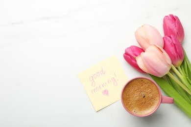 Cup of aromatic coffee, beautiful pink tulips and Good Morning note on white marble table, flat lay. Space for text