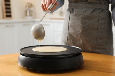 Photo of Woman cooking delicious crepe on electrical pancake maker in kitchen, closeup