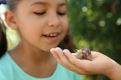 Kids playing with cute snails outdoors, focus on hand. Children spending time in nature
