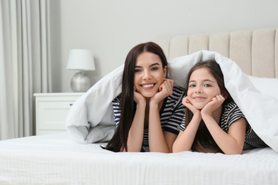 Young mother and her daughter under blanket in bed at home