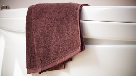 Brown soft towel on edge of bath indoors, closeup