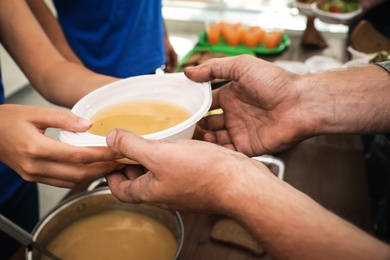 Volunteer serving food to poor people in charity centre, closeup