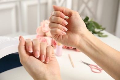 Woman doing manicure with ultraviolet nail lamp at white table, closeup