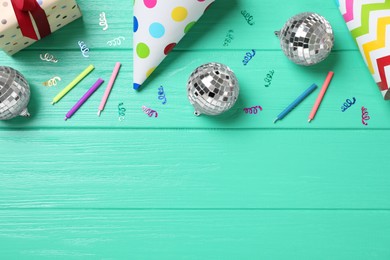 Shiny disco balls and party decor on turquoise wooden background, flat lay. Space for text