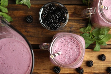 Photo of Tasty fresh milk shakes with blackberries on wooden table, flat lay