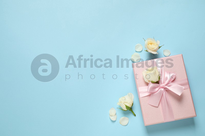 Pink gift box and beautiful flowers on light blue background, flat lay. Space for text