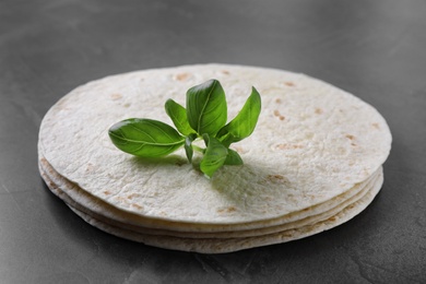 Stack of tasty tortillas with basil leaves on grey table, closeup