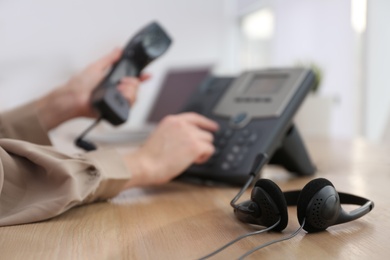 Woman using desktop telephone in office, focus on headset. Hotline service