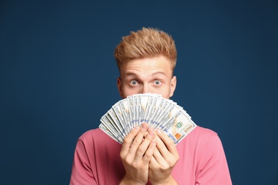 Portrait of surprised lottery winner with money fan on blue background