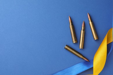 Ribbons in colors of national Ukrainian flag and bullets on blue background, flat lay. Space for text