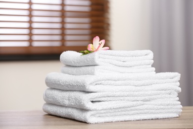 Pile of fresh towels and flower on wooden table in room