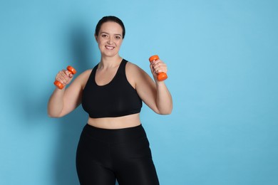 Happy overweight woman doing exercise with dumbbells on light blue background. Space for text
