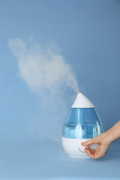 Woman using modern air humidifier on light blue background, closeup