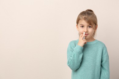 Sick little girl using nasal spray on beige background. Space for text