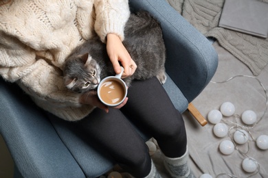 Woman in warm sweater with cute cat sitting in armchair, top view