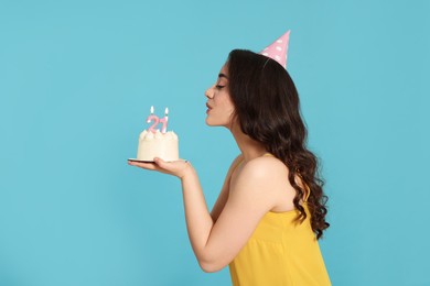Photo of Coming of age party - 21st birthday. Woman blowing number shaped candles on cake against light blue background