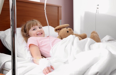Little child with intravenous drip and toy in hospital bed