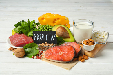 Photo of Card with word PROTEIN and different products on white wooden table