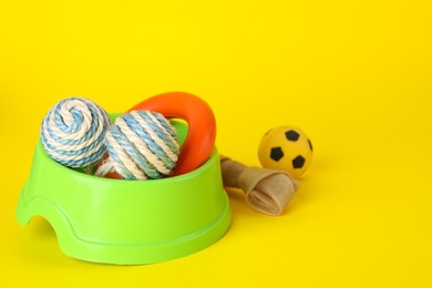 Various bright pet toys and bowl on yellow background, space for text