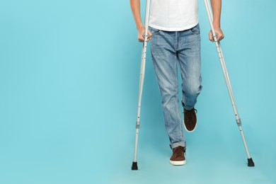 Man with injured leg using crutches on turquoise background, closeup. Space for text