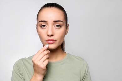 Photo of Woman with herpes applying cream on lips against light grey background. Space for text