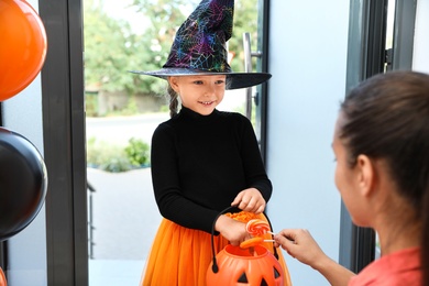 Cute little girl dressed as witch trick-or-treating at doorway. Halloween tradition