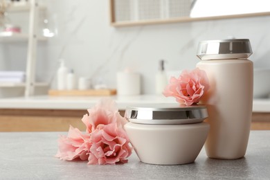 Hair care cosmetic products and beautiful flowers on light grey table in bathroom, space for text