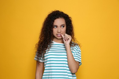 Photo of African-American woman biting her nails on yellow background