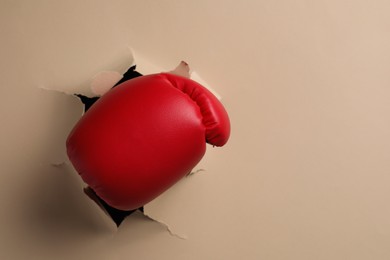 Man breaking through beige paper with boxing glove, closeup. Space for text