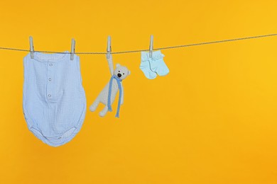 Baby clothes and toy drying on laundry line against orange background, space for text
