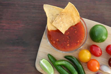 Photo of Tasty salsa sauce with tortilla chips and ingredients on wooden table, top view. Space for text