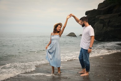 Happy young couple dancing on beach near sea. Space for text
