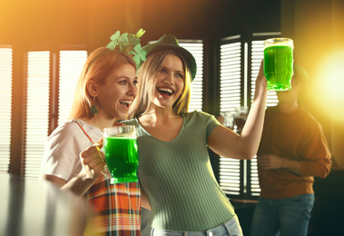 Young women with glasses of green beer in pub. St. Patrick's Day celebration
