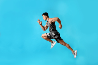 Athletic young man running on light blue background, side view