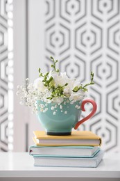 Beautiful bright flowers in cup and books on white table indoors