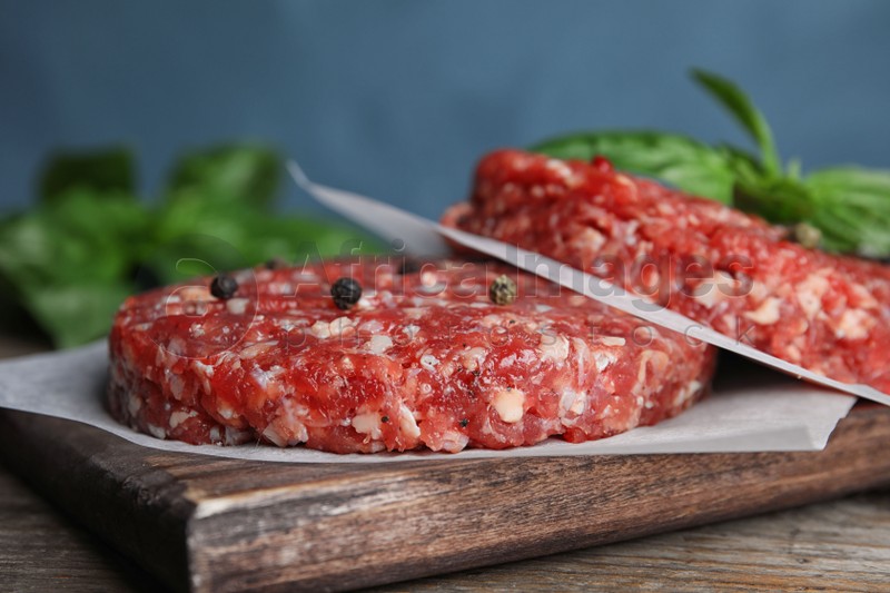 Raw meat cutlets for burger on wooden table against blue background, closeup