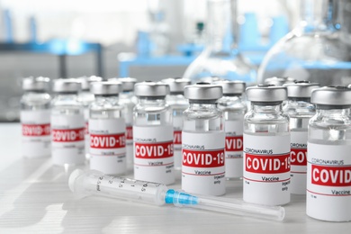 Glass vials with COVID-19 vaccine and syringe on white wooden table