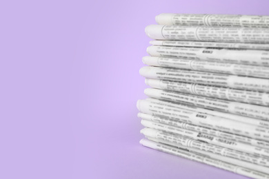 Stack of newspapers on light violet background, space for text. Journalist's work