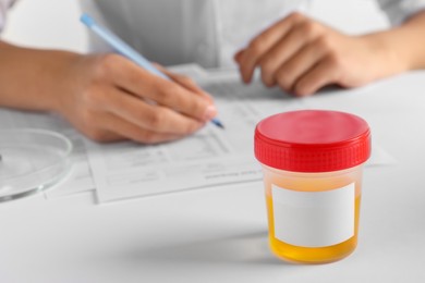 Closeup view of nurse writing urine analysis results at table, focus on container with sample