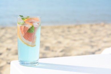 Photo of Glass of refreshing drink with grapefruit and mint on white table at beach, space for text