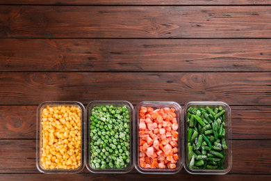 Different frozen vegetables on wooden table, flat lay. Space for text