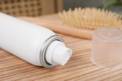Dry shampoo spray near hairbrush on wooden table indoors, closeup