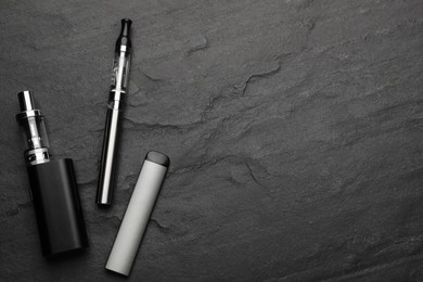 Electronic smoking devices on black background, flat lay. Space for text