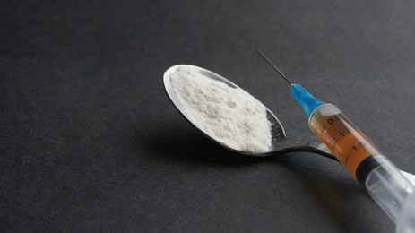 Photo of Spoon with powder, syringe on black background, closeup and space for text. Hard drugs