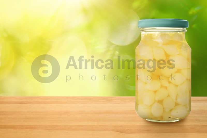 Jar of pickled onion bulbs on wooden table against blurred background, space for text