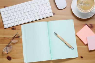 Empty notebook, keyboard, coffee and stationery on wooden table, flat lay